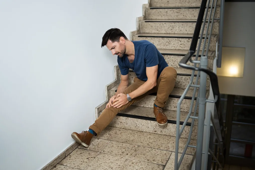 Man sitting on stairs holding his knee in pain. If you’ve sustained an injury on someone’s property, contact our Houston slip & fall lawyers today.