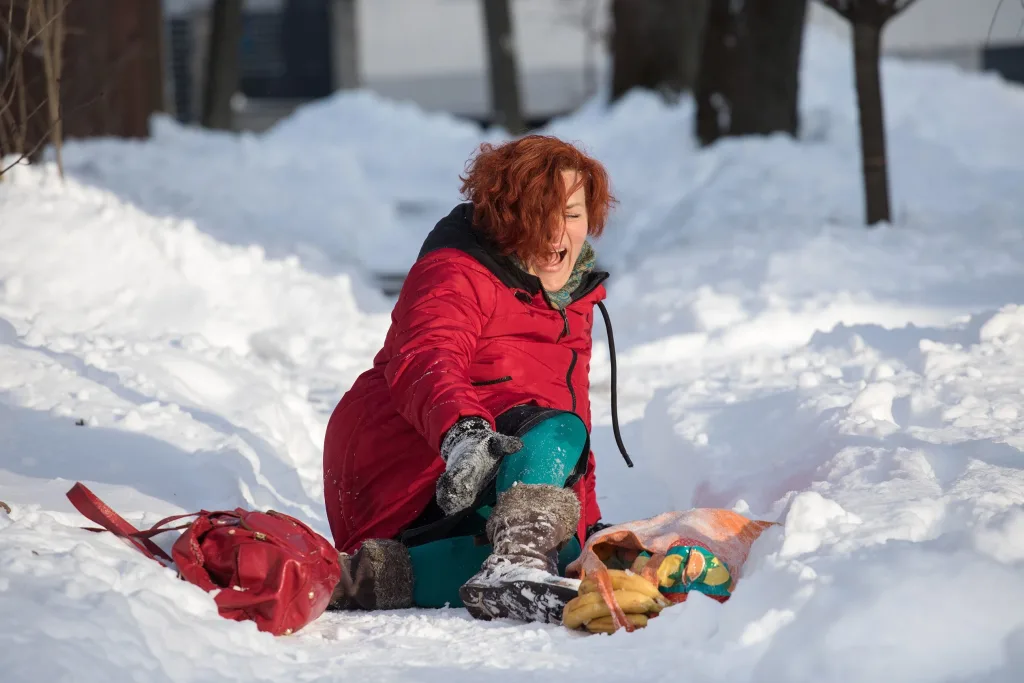Woman sitting on the ground in the snow crying in pain and holding her leg. If you’ve been injured on someone’s property due to snow or ice, contact our Houston premises liability attorneys today.