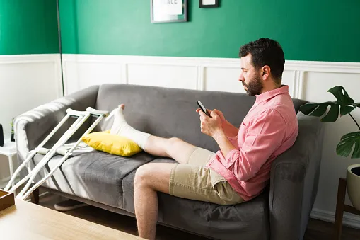 A man with an injured leg sitting on his couch on his phone.