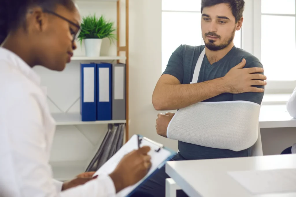 A man with an arm in a sling talking to his doctor.