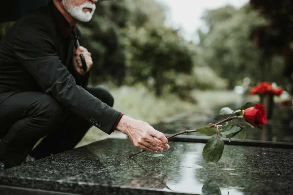 A man laying a rose down on a grave.
