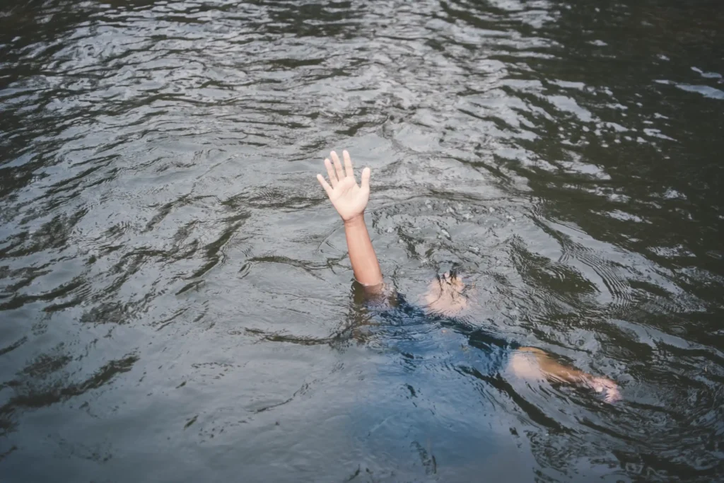 A drowning boy with his arm out of water at the lake.