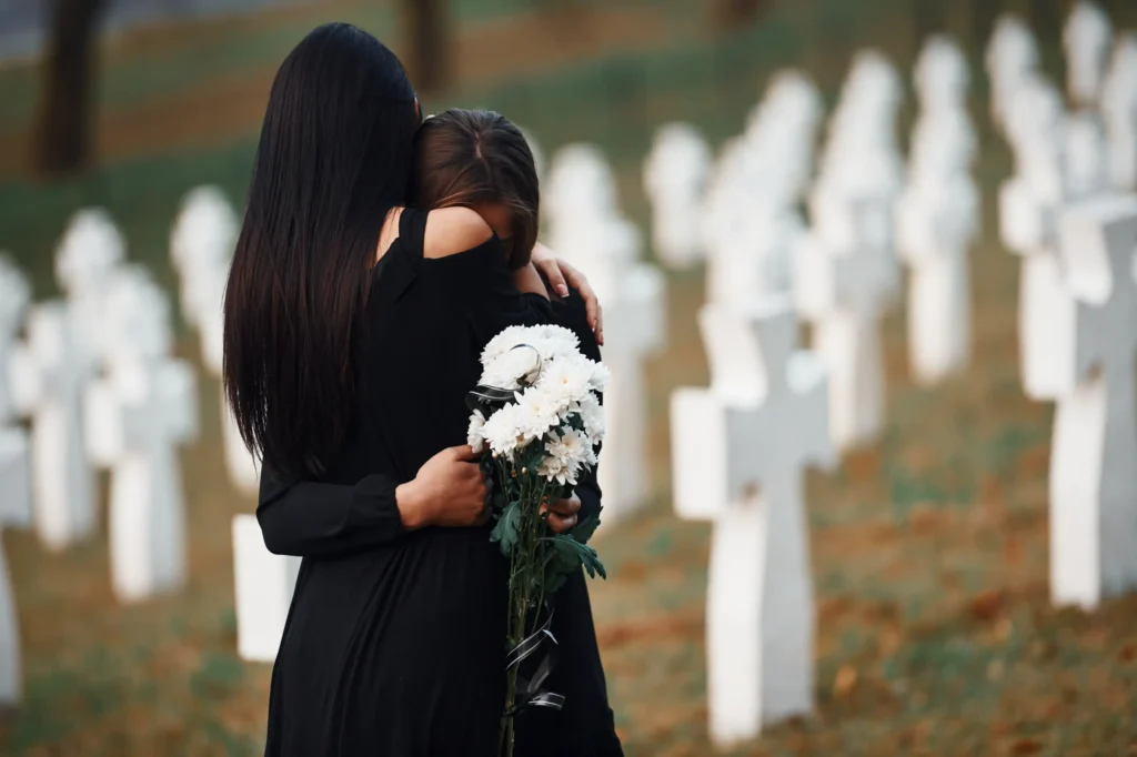 Two young women in black clothes visiting cemetery with many white crosses. 